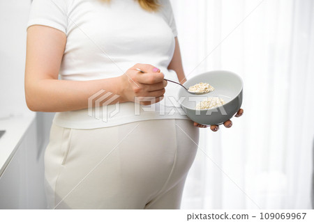 Pregnant woman holding a plate of oatmeal in the kitchen  109069967