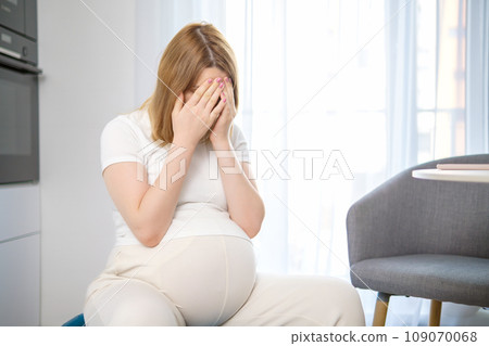 Tired pregnant woman closes her face with her hands.  109070068