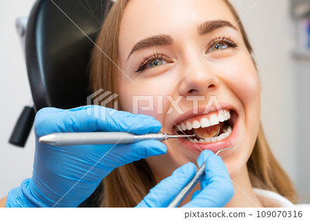 The dentist, wearing gloves, uses a small mirror and dental probe to inspect the patients teeth and gums 109070316