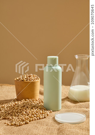 Cosmetic bottle displayed with a bowl of soybeans. A conical flask and petri dish of soybean milk featured. Natural cosmetic concept. Empty label for branding mockup Cosmetic bottle displayed with a bowl of soybeans. A conical flask and petri dish of soybean milk featured. Natural cosmetic concept. Empty label for branding mockup 109070645