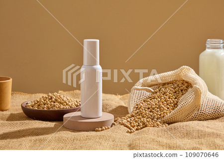 Round podium with a white bottle standing on. Mesh bag and wooden dish containing lots of soybeans displayed. Natural beauty blank label for branding mock-up concept Round podium with a white bottle standing on. Mesh bag and wooden dish containing lots of soybeans displayed. Natural beauty blank label for branding mock-up concept 109070646