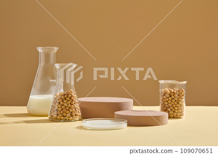 Erlenmeyer flasks, petri dish and a beaker containing soybeans and milk arranged with brown podiums. Mock-up for exhibitions or presentation of cosmetic products or packaging 109070651