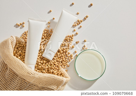Soybean seeds and two unlabeled tubes displayed with a petri dish filled with soybean milk. White cosmetic tube for face cream, cleanser, body lotion or shampoo 109070668