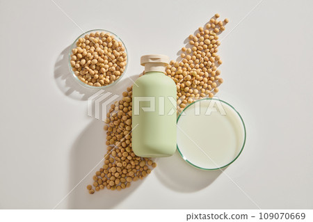 Cosmetic bottle without label placed on a heap of soybeans, displayed with two petri dishes. Soybean benefits include skin brightening and reducing redness from sun exposure 109070669