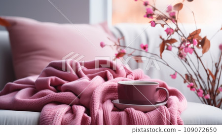 Fragment of modern cozy living room in pink colors. Comfortable sofa with cushions and soft plaid, branches with pink flowers in a vase, tea cup and saucer. Beautiful light from the window. Fragment of modern cozy living room in pink colors. Comfortable sofa with cushions and soft plaid, branches with pink flowers in a vase, tea cup and saucer. Beautiful light from the window. 109072650