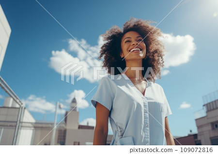Half-length portrait of young charming African American woman in casual clothes outdoors against the summer blue sky. Beautiful black girl with afro hairstyle looking up and smiling happily. Half-length portrait of young charming African American woman in casual clothes outdoors against the summer blue sky. Beautiful black girl with afro hairstyle looking up and smiling happily. 109072816