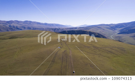 A white SUV rides in the mountains through fields A white SUV rides in the mountains through fields 109074313