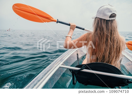 Woman in kayak back view. Happy young woman with long hair floating in transparent kayak on the crystal clear sea. Summer holiday vacation and cheerful female people relaxing having fun on the boat 109074710