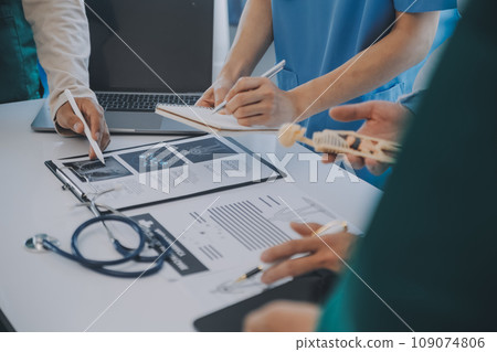 Multiracial medical team having a meeting with doctors in white lab coats and surgical scrubs seated at a table discussing a patients records Multiracial medical team having a meeting with doctors in white lab coats and surgical scrubs seated at a table discussing a patients records 109074806
