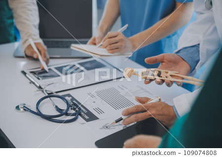 Multiracial medical team having a meeting with doctors in white lab coats and surgical scrubs seated at a table discussing a patients records Multiracial medical team having a meeting with doctors in white lab coats and surgical scrubs seated at a table discussing a patients records 109074808