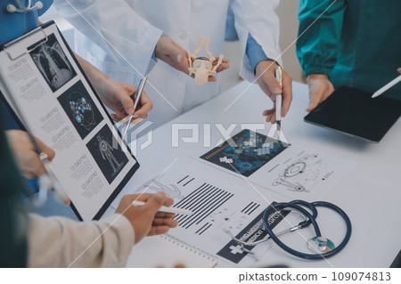 Multiracial medical team having a meeting with doctors in white lab coats and surgical scrubs seated at a table discussing a patients records Multiracial medical team having a meeting with doctors in white lab coats and surgical scrubs seated at a table discussing a patients records 109074813
