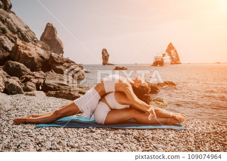 Woman sea yoga. Two happy women practicing yoga on the beach with ocean and rock mountains. Motivation and inspirational fit and exercising. Healthy lifestyle outdoors in nature, fitness concept. 109074964
