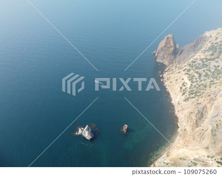 Aerial view from above on calm azure sea and volcanic rocky shores. Small waves on water surface in motion blur. Nature summer ocean sea beach background. Nobody. Holiday, vacation and travel concept 109075260