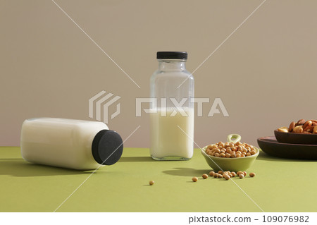 Two blank label bottle of soybean milk decorated on green surface with a dish of soybean seeds. Wooden dish containing some nuts. Soy is a very special ingredient 109076982