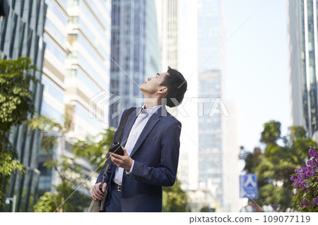 young asian business man looking up at tall buildings in downtown young asian business man looking up at tall buildings in downtown 109077119