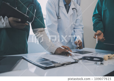 Multiracial team of doctors discussing a patient standing grouped in the foyer looking at a tablet computer, close up view 109077615