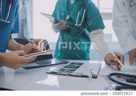 Multiracial team of doctors discussing a patient standing grouped in the foyer looking at a tablet computer, close up view 109077617