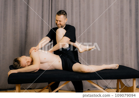 Man professional doctor osteopath fixing and stretching mans back with hands during exersicing at rehabilitation theapy in manual therapy clinic, top view. Chiropractor during work Man professional doctor osteopath fixing and stretching mans back with hands during exersicing at rehabilitation theapy in manual therapy clinic, top view. Chiropractor during work 109079094