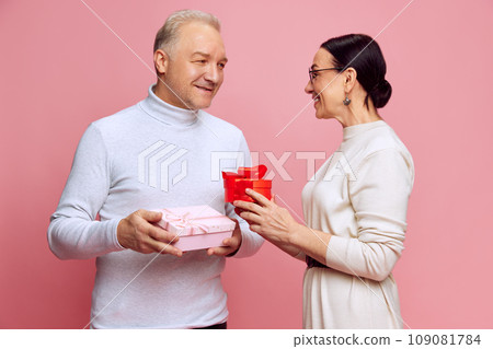Senior man and woman, married couple giving each other presents, celebrating holiday, anniversary against pink studio background. Valentine's Day 109081784