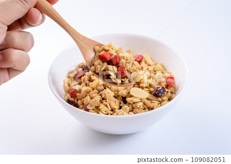 Scooping cereal in a white plate with a spoon, fruit granola, breakfast, health food, overhead view, white background 109082051