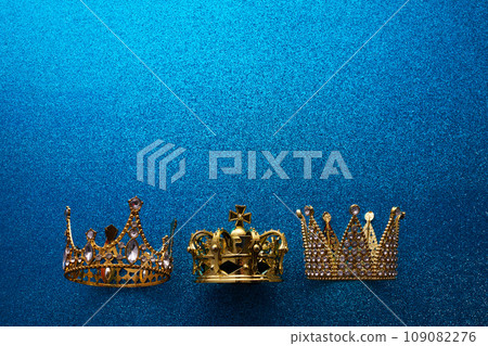 Epiphany Day or Dia de Reyes Magos concept. Three gold crowns on blue sparkling background Epiphany Day or Dia de Reyes Magos concept. Three gold crowns on blue sparkling background 109082276