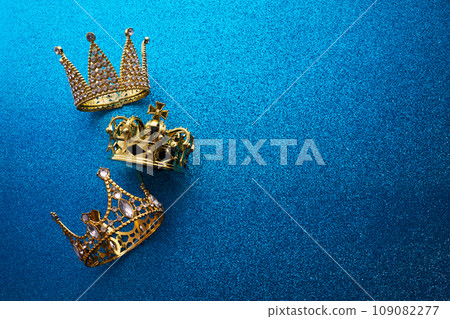 Epiphany Day or Dia de Reyes Magos concept. Three gold crowns on blue sparkling background Epiphany Day or Dia de Reyes Magos concept. Three gold crowns on blue sparkling background 109082277