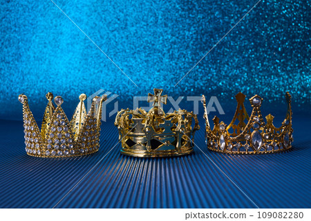 Epiphany Day or Dia de Reyes Magos concept. Three gold crowns on blue sparkling background Epiphany Day or Dia de Reyes Magos concept. Three gold crowns on blue sparkling background 109082280