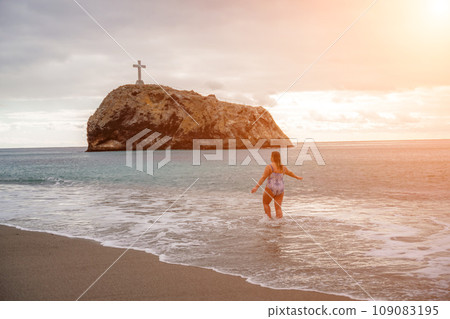 A plump woman in a bathing suit enters the water during the surf A plump woman in a bathing suit enters the water during the surf 109083195