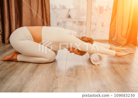 Adult athletic woman, in white bodysuit, performing fascia exercises on the floor - caucasian woman using a massage foam roller - a tool to relieve tension in the back and relieve muscle pain - the Adult athletic woman, in white bodysuit, performing fascia exercises on the floor - caucasian woman using a massage foam roller - a tool to relieve tension in the back and relieve muscle pain - the 109083230