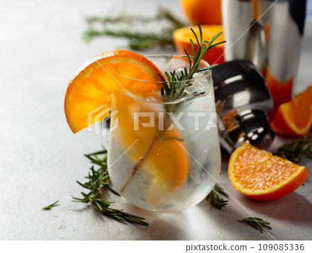 Refreshing drink with natural ice, orange, and rosemary in a frozen glass. 109085336