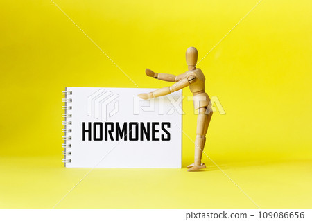 HORMONES written on a notepad on a yellow background held by a wooden doll. Medical concept 109086656