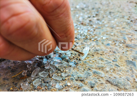The fingers of the hand hold a small rod and poke at a small white object that lies on the ground among the shards of glass The fingers of the hand hold a small rod and poke at a small white object that lies on the ground among the shards of glass 109087263