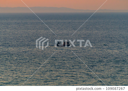 A fishing boat catches fish with nets in the ocean on the sunset horizon. Partial defocus, haze, fog. The concept of the use of natural resources, food, technology A fishing boat catches fish with nets in the ocean on the sunset horizon. Partial defocus, haze, fog. The concept of the use of natural resources, food, technology 109087267