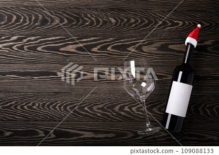 Santa hat on bottle with red wineand glass on wooden rustic background. Christmas celebration. New year decoration Santa hat on bottle with red wineand glass on wooden rustic background. Christmas celebration. New year decoration 109088133