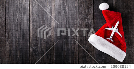 Airplane on Santa Claus hat on wooden rustic background. Christmas celebration. Long banner Airplane on Santa Claus hat on wooden rustic background. Christmas celebration. Long banner 109088134