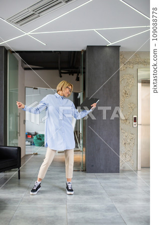 Well done woman successfully completed project, blonde businesswoman dancing outside office building in corridor at workplace. 109088778