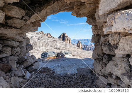 View of the rifugio Boe mountain hut through a stone window in the cairn. Dolomites, Italian Alps. Sella massif View of the rifugio Boe mountain hut through a stone window in the cairn. Dolomites, Italian Alps. Sella massif 109091213