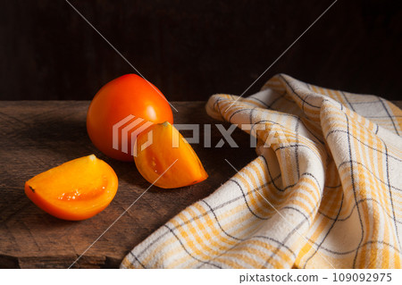 Cut and whole of yellow tomato and yellow towel on wooden background.. Cut and whole of yellow tomato and yellow towel on wooden background.. 109092975