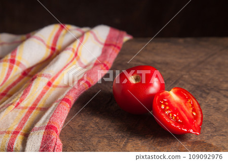 Whole and half of pink tomato and red towel on wooden background.. Whole and half of pink tomato and red towel on wooden background.. 109092976