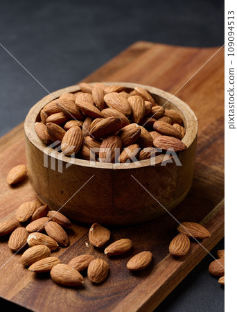 Peeled almond kernels in a round wooden plate on the table 109094513