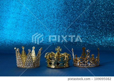 Epiphany Day or Dia de Reyes Magos concept. Three gold crowns on blue sparkling background Epiphany Day or Dia de Reyes Magos concept. Three gold crowns on blue sparkling background 109095082