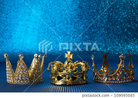 Epiphany Day or Dia de Reyes Magos concept. Three gold crowns on blue sparkling background Epiphany Day or Dia de Reyes Magos concept. Three gold crowns on blue sparkling background 109095085