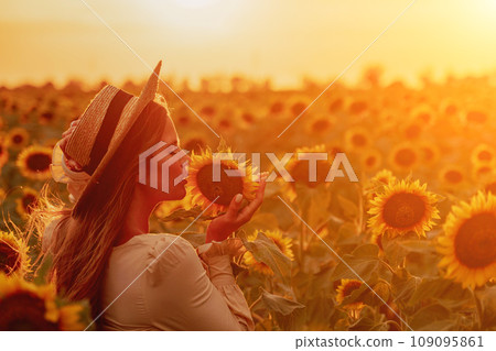 Woman in Sunflower Field: Happy girl in a straw hat posing in a vast field of sunflowers at sunset, enjoy taking picture outdoors for memories. Summer time. Woman in Sunflower Field: Happy girl in a straw hat posing in a vast field of sunflowers at sunset, enjoy taking picture outdoors for memories. Summer time. 109095861