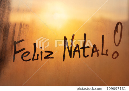 Congratulation lettering Portuguese Feliz i\Natal is Merry Christmas in english on muddy wet orange window in city on sunset 109097181