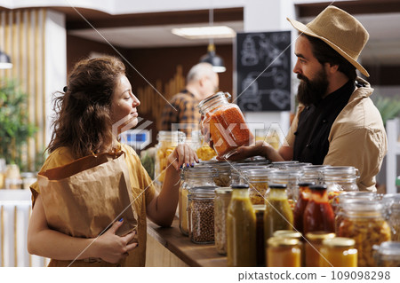 Zero waste shop entrepreneur showing his natural chemical free products to customer interested in low planet impact lifestyle. Ecofriendly supermarket owner presenting his merchandise to client Zero waste shop entrepreneur showing his natural chemical free products to customer interested in low planet impact lifestyle. Ecofriendly supermarket owner presenting his merchandise to client 109098298