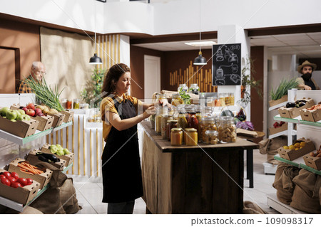 Vendor arranging products sold in bulk in zero waste store, minimizing plastic usage, creating positive environmental impact. Seller preparing ethically sourced pantry staples for incoming customers Vendor arranging products sold in bulk in zero waste store, minimizing plastic usage, creating positive environmental impact. Seller preparing ethically sourced pantry staples for incoming customers 109098317