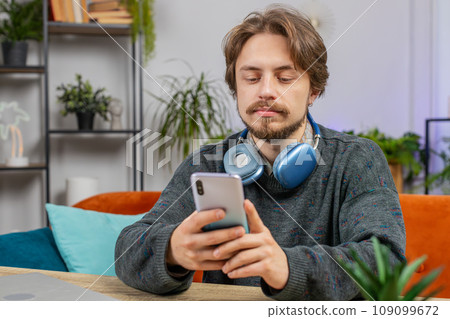 Caucasian bearded man sitting at table use smartphone share messages on social media application 109099672