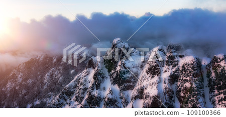 Mountain Peak Covered in Snow. Winter Season. Cloudy Sunset. Aerial View. Mountain Peak Covered in Snow. Winter Season. Cloudy Sunset. Aerial View. 109100366