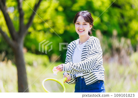 Smiling young woman enjoying badminton outdoors 109101823