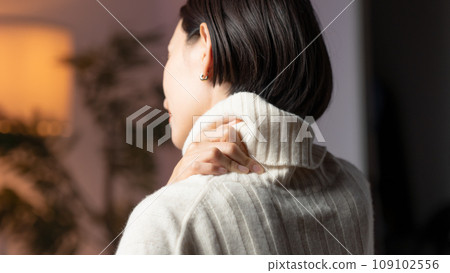 A woman holding her shoulder in a room 109102556